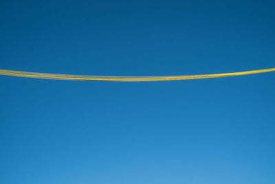 Low angle view of yellow cables against clear blue sky