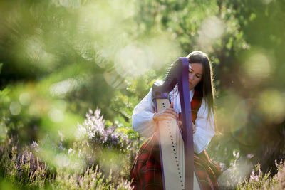 Woman playing harp against trees in forest