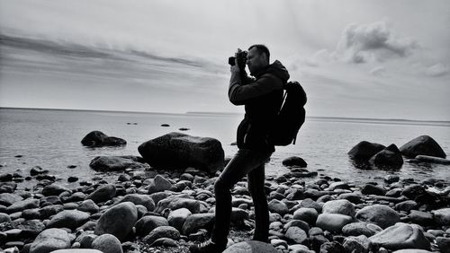 Side view of man photographing on at beach against sky