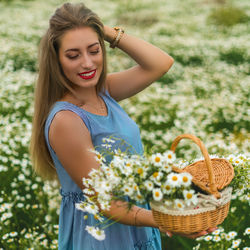 Beautiful young woman holding basket while standing against wall