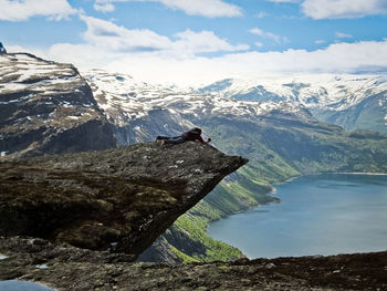 Man lying on cliff by over lake against sky
