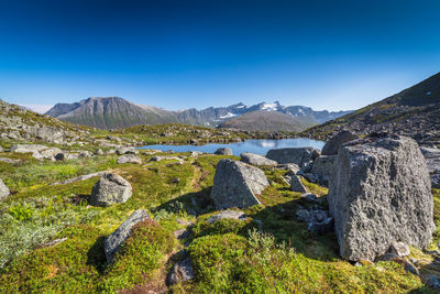 Pond surrounded by rocks and mountains against clear sky