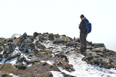 Rear view of man standing on rock against clear sky