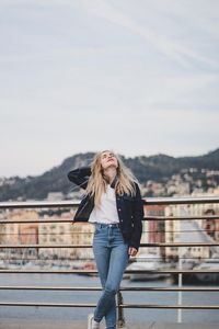 Full length of woman standing on railing against sky