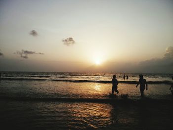 Silhouette people walking on calm beach at sunset