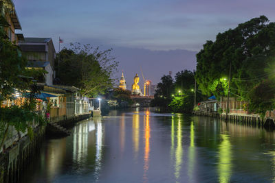 River by illuminated buildings against sky