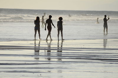 People at beach against sky during sunset