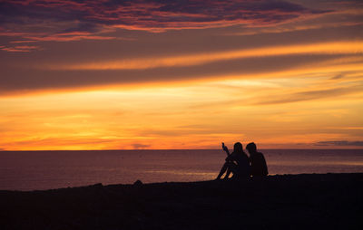 Silhouette people on beach against sky during sunset