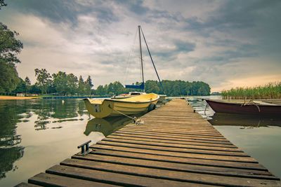 Boats moored at harbor by lake against sky