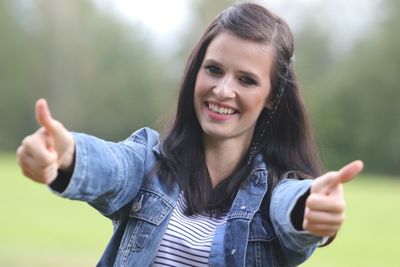 Portrait of smiling young woman gesturing thumbs up against trees