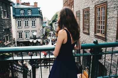 Rear view of woman standing by railing in city