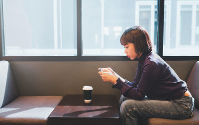 Young man using mobile phone while sitting on window