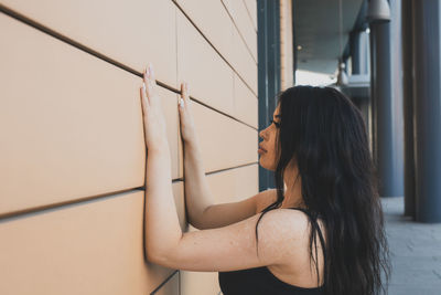 Side view of young woman touching wall while standing outdoors