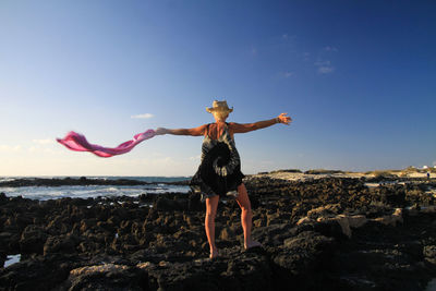 Woman standing on rock at sea shore against sky