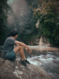 Side view of young man sitting on rock in forest