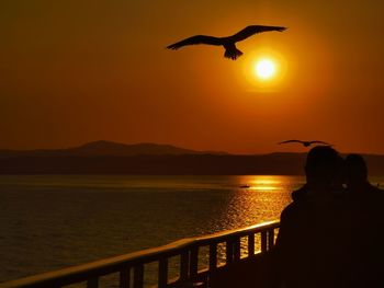 Rear view of silhouette woman standing by sea against sky during sunset