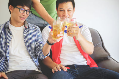 Men toasting beer glasses while watching tv at home