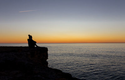 Silhouette person standing on rock against sea during sunset