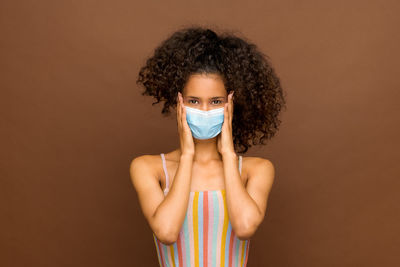 Portrait of woman wearing mask standing against colored background