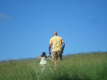 Rear view of father and daughter walking on field against clear sky