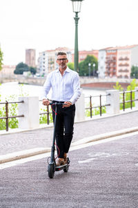 Young businessman in a suit riding an electric scooter while commuting to work in city