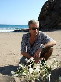 Young man sitting on beach against clear sky