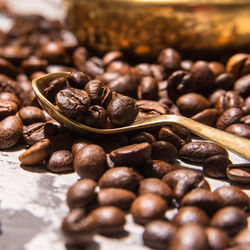 Coffee beans in a spoon and scattered on the table, close-up, space for text