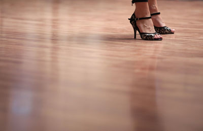 Low section of woman wearing high heels standing on hardwood floor
