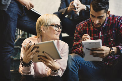 Business people with notepad and digital tablet sitting on steps in office