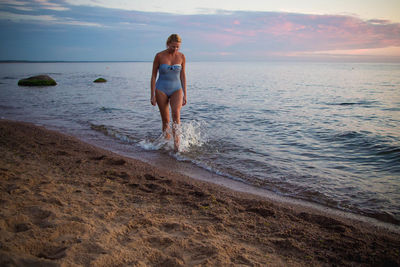 Woman standing on beach against sky during sunset