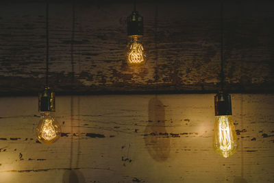 Close-up of illuminated light bulb hanging on wall