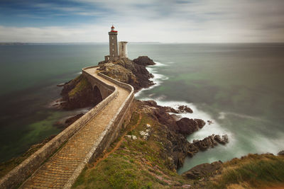 Lighthouse on pier by sea against sky