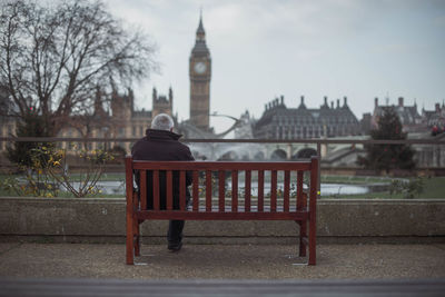 Man on bench in city against sky