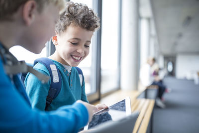 Smiling pupils sharing a tablet on school corridor