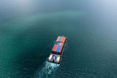 Aerial view small container ship sending goods sailing in green sea