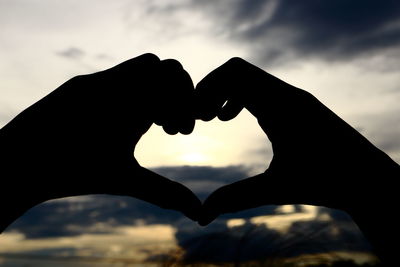 Cropped hands of couple making heart shape against sky
