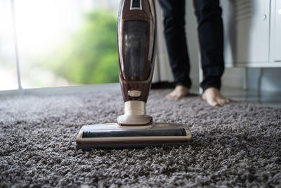 Low section of person cleaning carpet with vacuum cleaner at home
