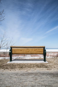 Bench on snow covered field against sky