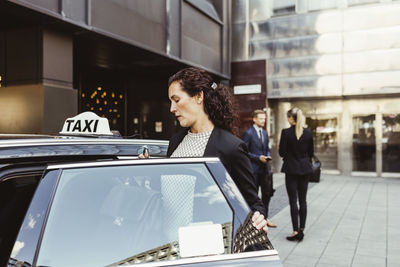 Female entrepreneur entering in taxi while coworkers standing in background