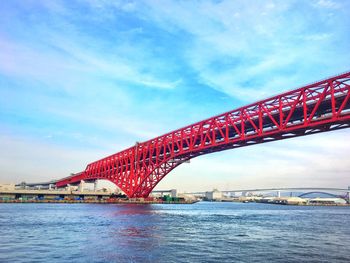 Low angle view of red bridge over river against cloudy sky