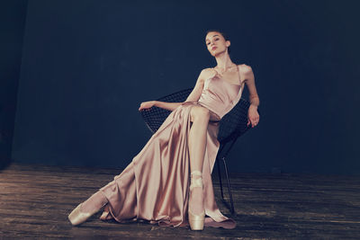 Portrait of a ballerina in a pink dress is sitting on a chair with her leg in the slit of the dress