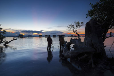 Silhouette man and woman by sea during sunset