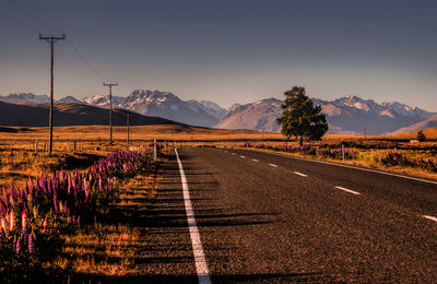 Empty road amidst field against snowcapped mountains