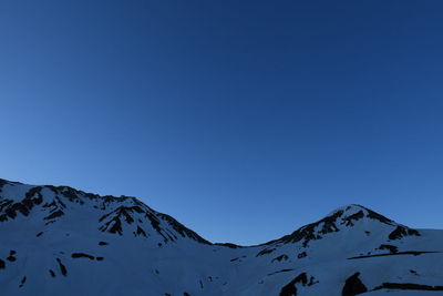 Low angle view of snowcapped mountains against clear blue sky