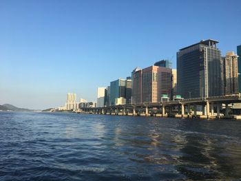 Sea by modern buildings against clear blue sky