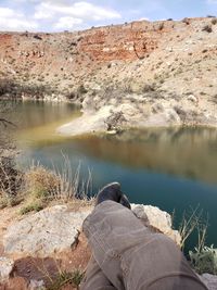 Low section of man relaxing on rock by lake