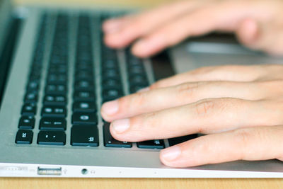 Cropped hands of person using laptop on wooden table