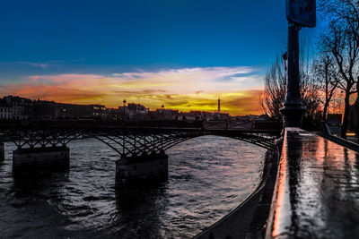 Bridge over river in city against sky at sunset