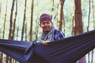 Low angle view of young man holding hammock in forest