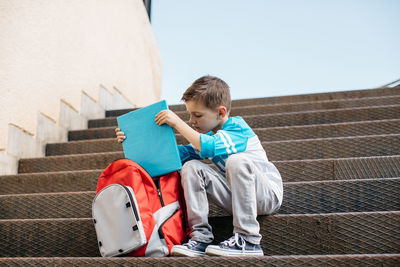 Boy putting book in bag while sitting on steps